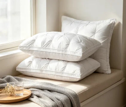 A stack of white hotel-grade memory foam sleeping pillows resting on a light-colored surface next to a window.