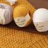 A close-up of two skeins of wool thread, one yellow and one white, resting on a woven yellow background.