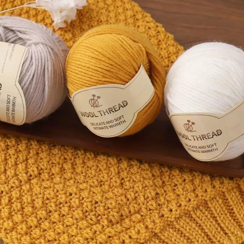 A close-up of two skeins of wool thread, one yellow and one white, resting on a woven yellow background.