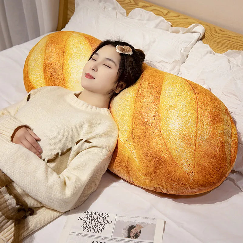 A woman rests her head on a large, golden-yellow plush baguette shaped pillow while wearing a cream sweater.