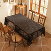 An elegant black lace tablecloth with floral embroidery is spread over a wooden table in a sunlit room.
