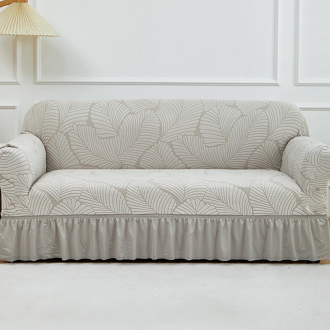 A beige jacquard stretch sofa cover featuring a leaf pattern on a light gray sofa.