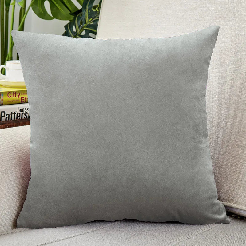A square, soft gray velvet cushion cover resting on a light-colored surface.