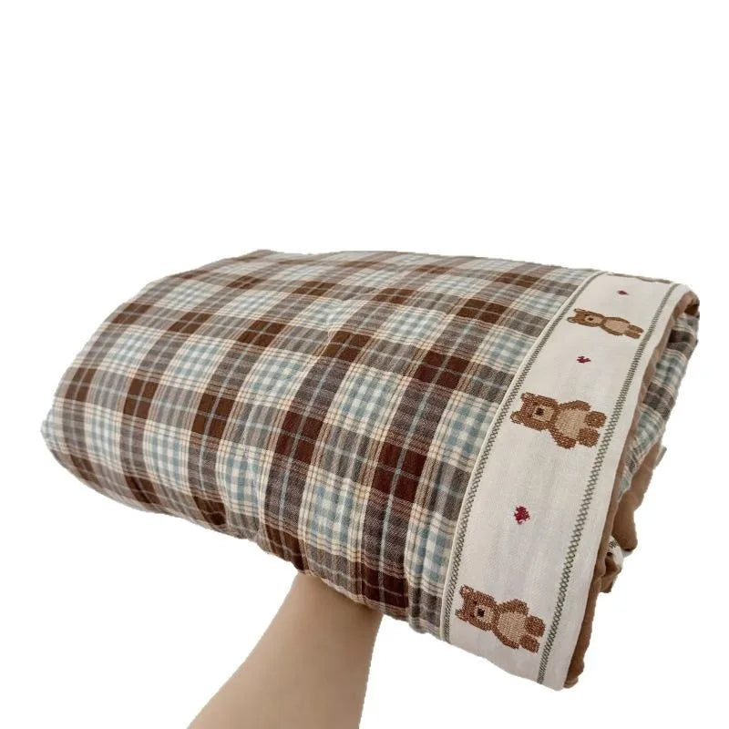 A plaid muslin blanket with floral print trim folded and displayed.