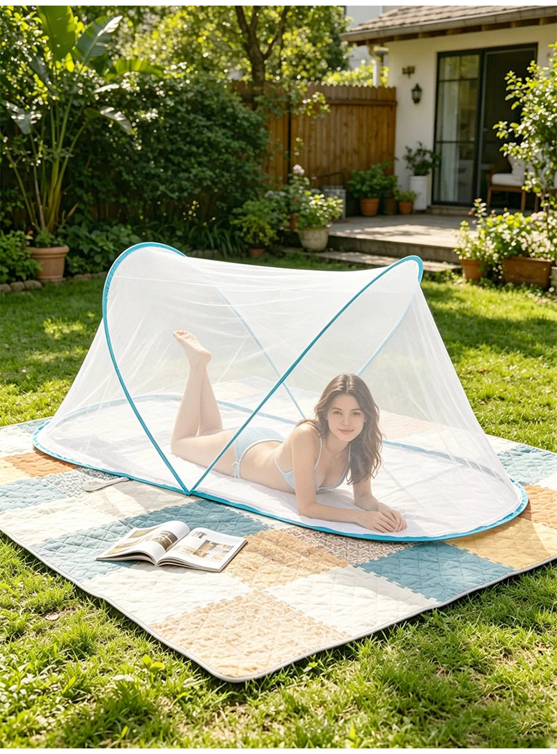 A woman relaxing on a portable mosquito net spread out on a mat in a grassy outdoor setting.