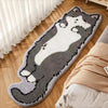A gray and white cartoon cat plush rug lying on a wooden floor next to a bed with a beige blanket.