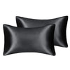 A set of three black silky satin pillow covers, including a standard and a larger queen size pillow.