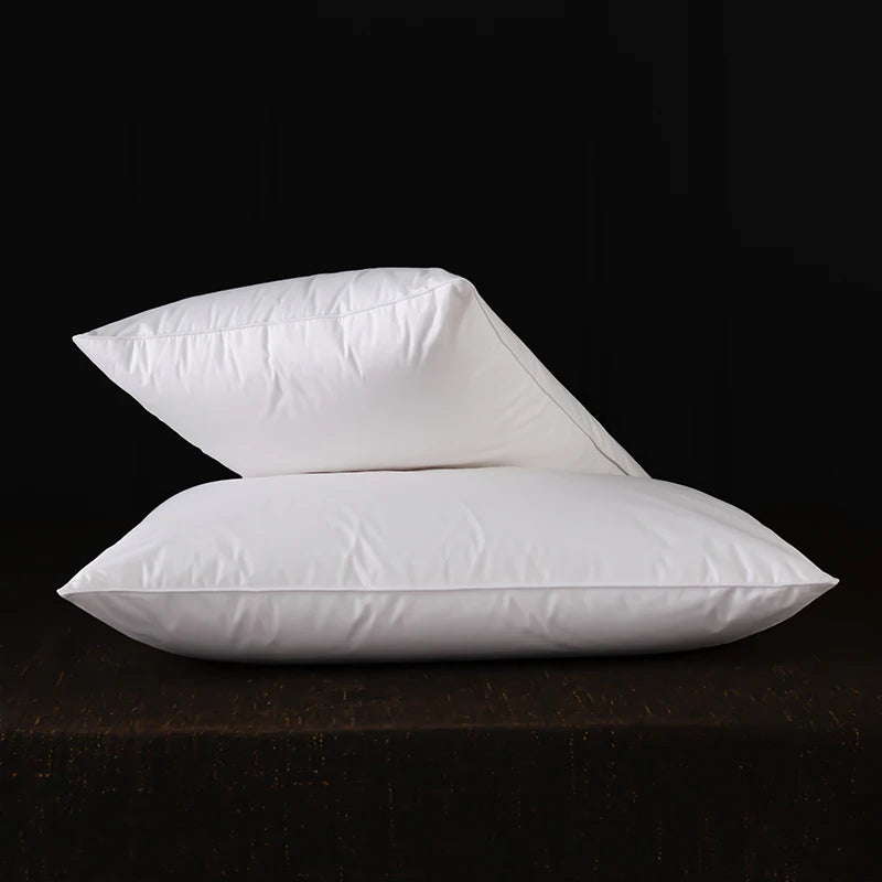 A stack of white natural goose down and feather sleeping pillows resting on a dark surface.