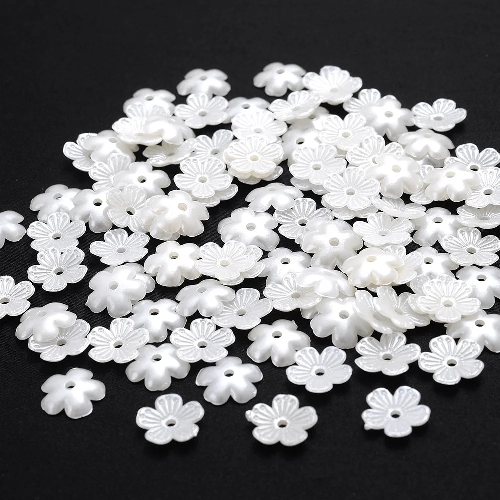 A pile of small, white imitation pearl flower spacer beads for DIY jewelry.
