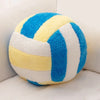 A plush volleyball ball cushion with blue and yellow stripes resting on a white surface.