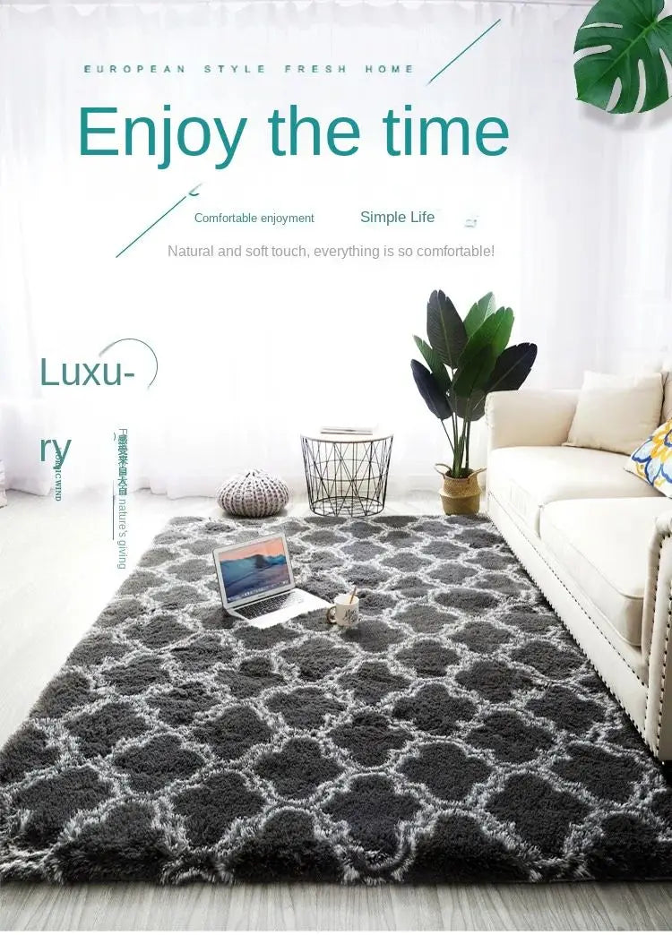 A dark gray geometric plush area rug is displayed on a light wooden floor in a bright living room setting.