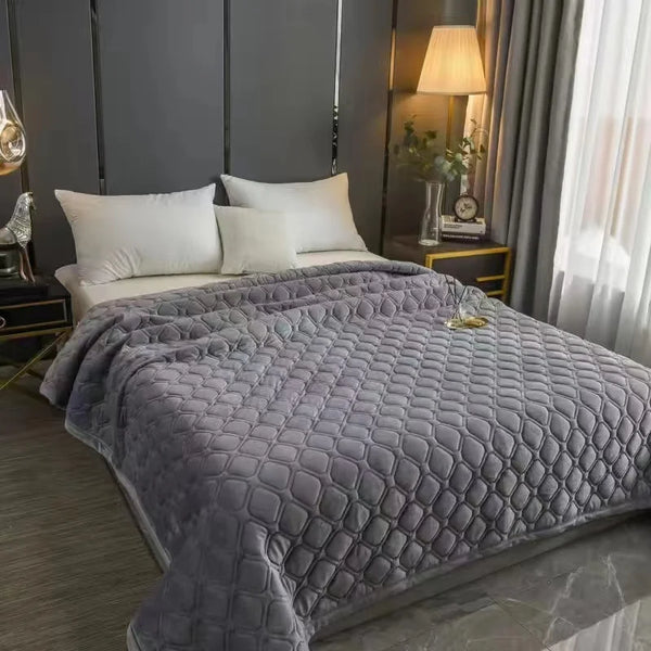 A gray plush velvet quilted bed cover blanket draped over a bed in a modern bedroom setting.
