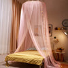 Pink sheer mosquito net canopy draped over a bed in a bedroom setting.