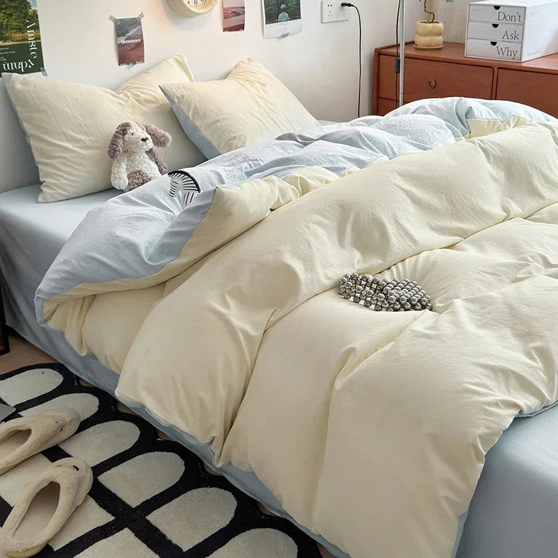 A bed covered with a beige quilt and white pillows, featuring a light blue duvet and a small stuffed animal.