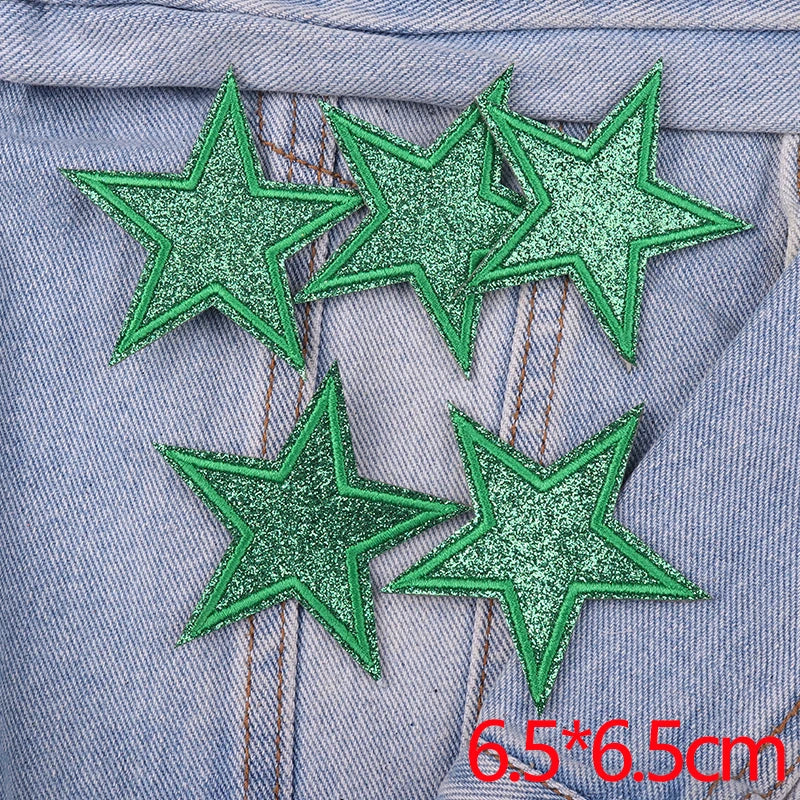 Five green glitter star patches are placed on a denim fabric background.