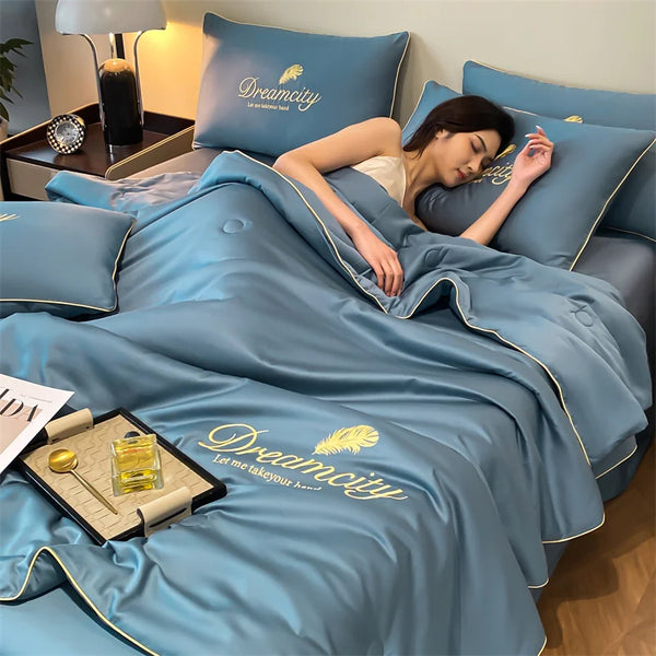A woman is relaxing on a blue Dreamcity quilt in bed, with pillows and a bedside lamp visible.