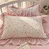 A white pillow with pink floral embroidery and ruffled fabric on a pink bed.