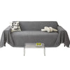 A gray sofa covered with a waterproof chenille slipcover, featuring a white pillow and a rolled white decorative item.