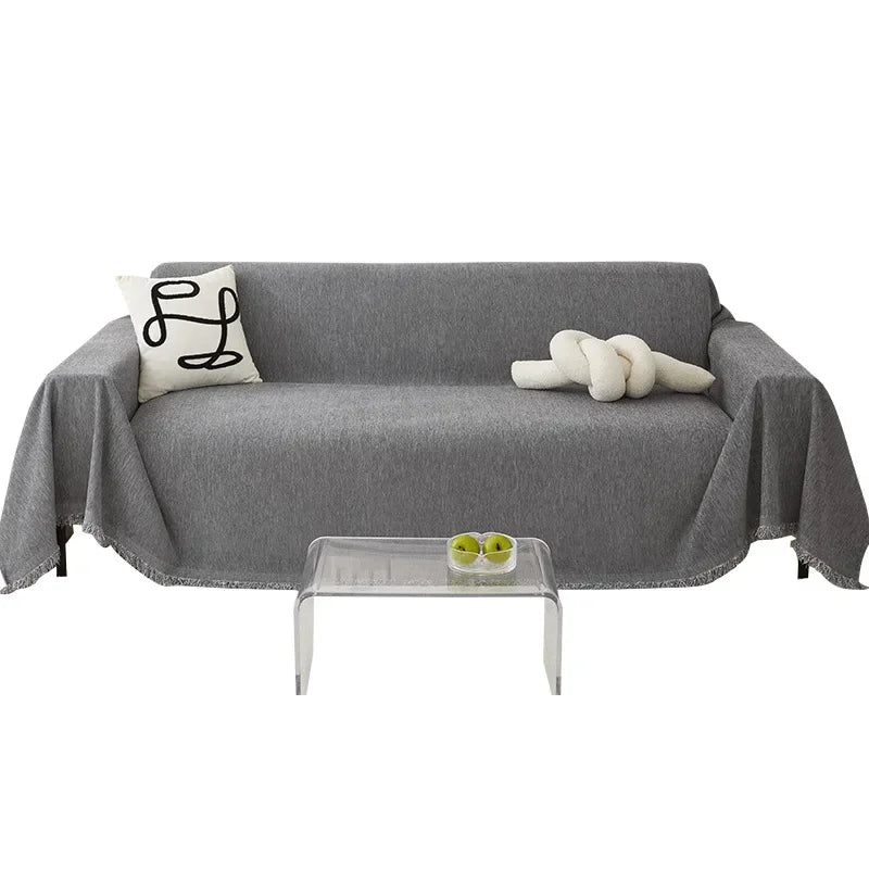 A gray sofa covered with a waterproof chenille slipcover, featuring a white pillow and a rolled white decorative item.