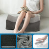 A person is sitting and using an ergonomic memory foam leg support pillow, showing the sponge texture and fabric.