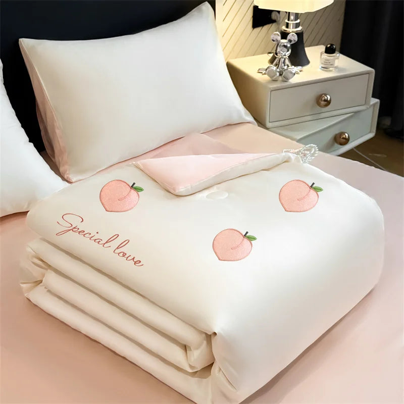 A white embroidered cooling summer quilt folded neatly on a pink surface with a pillow and a decorative box in the background