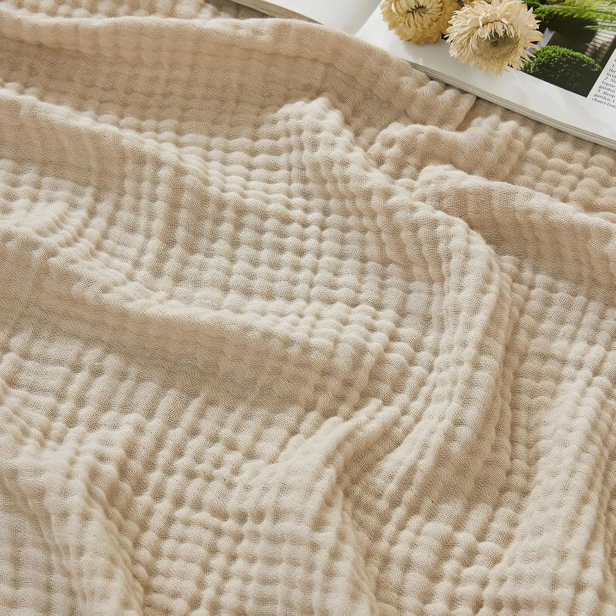 A beige muslin blanket with a textured, quilted pattern is draped softly on a surface.