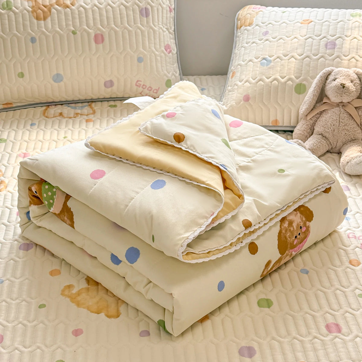 A stack of cream-colored quilted blankets with a subtle pattern rests on a light yellow textured surface next to a stuffed an