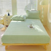 A light green flannel fitted sheet with a white gingham pattern is laid out on a wooden bed frame.