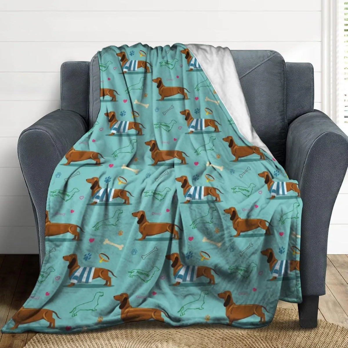 A teal flannel blanket featuring a pattern of brown and white dachshunds on a gray armchair.