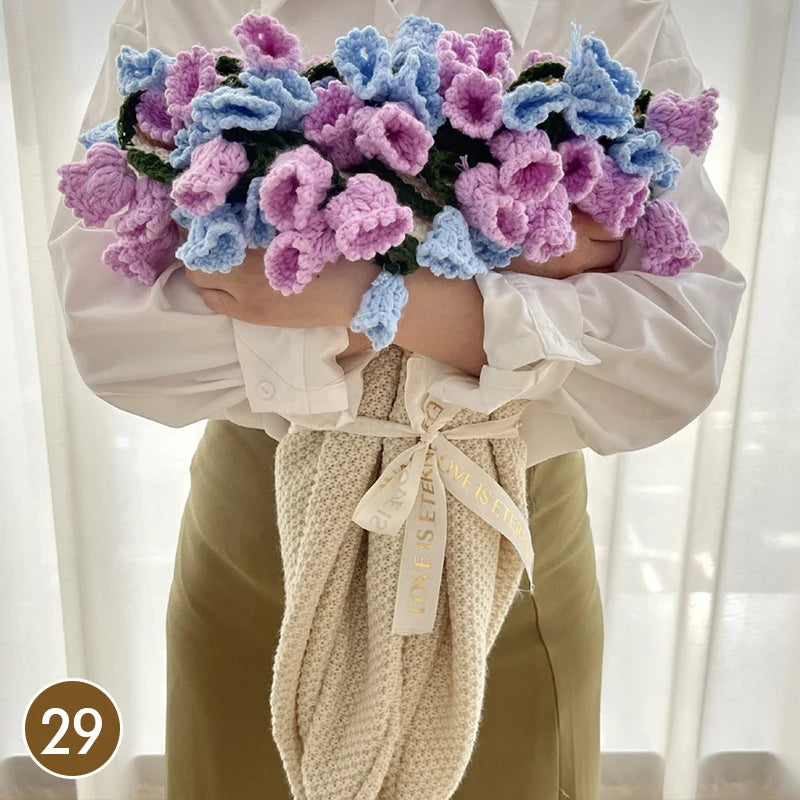 A hand knitted floral rose bouquet throw blanket is held by a person, featuring purple and blue flowers.