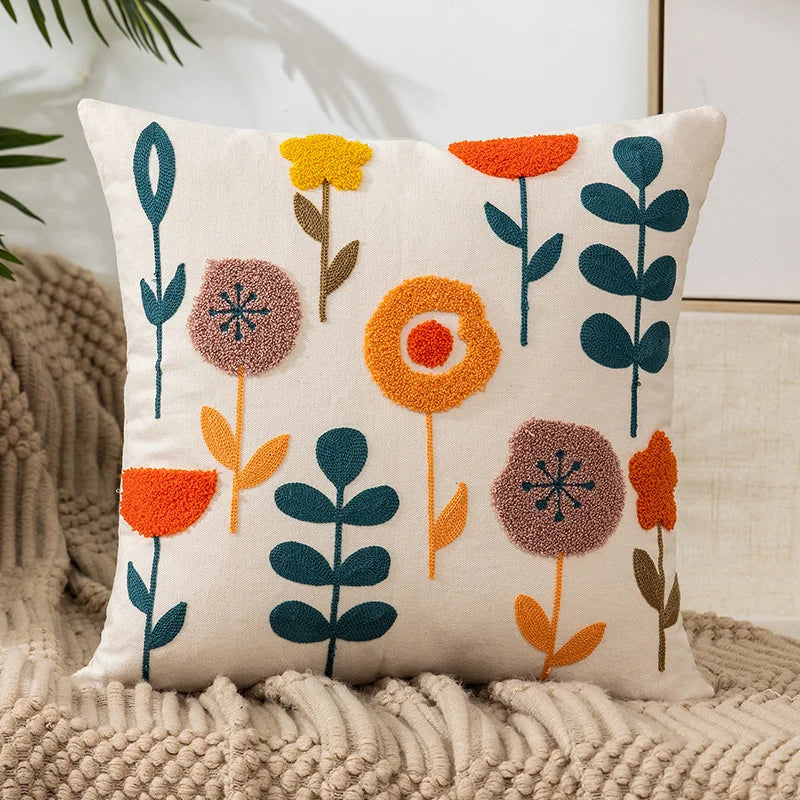 A cream-colored throw pillow cover embroidered with various colored floral designs like orange, yellow, and deep blue.