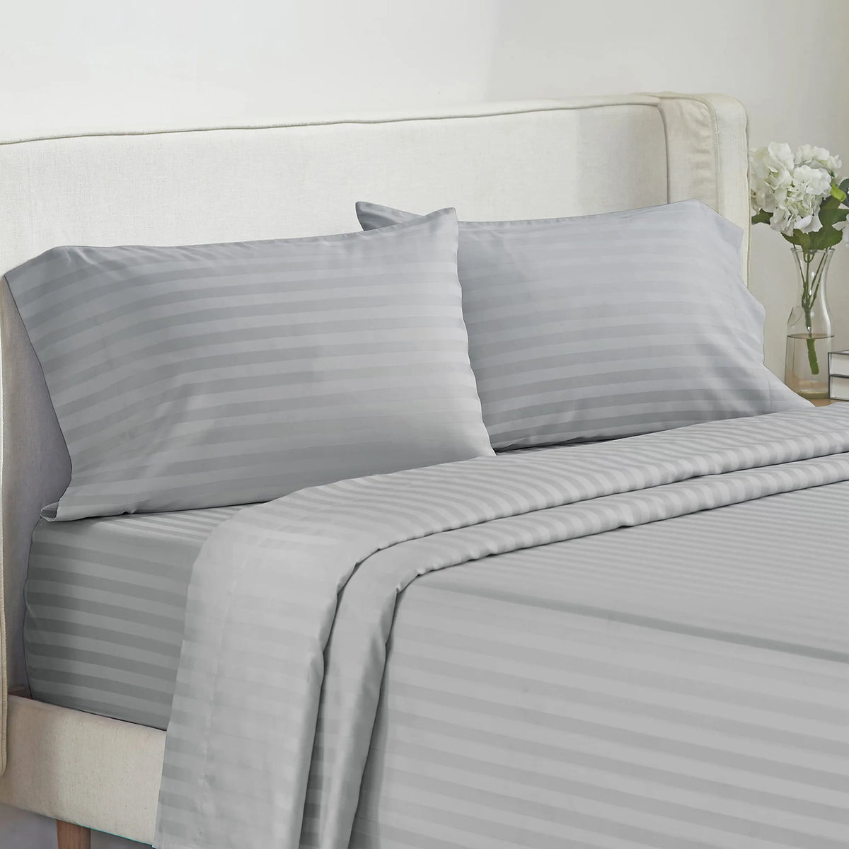 A set of gray and white striped luxury bedding, including pillows and a duvet cover, on a bed.