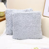 A stack of fluffy gray velvet throw pillow covers resting on a white surface.
