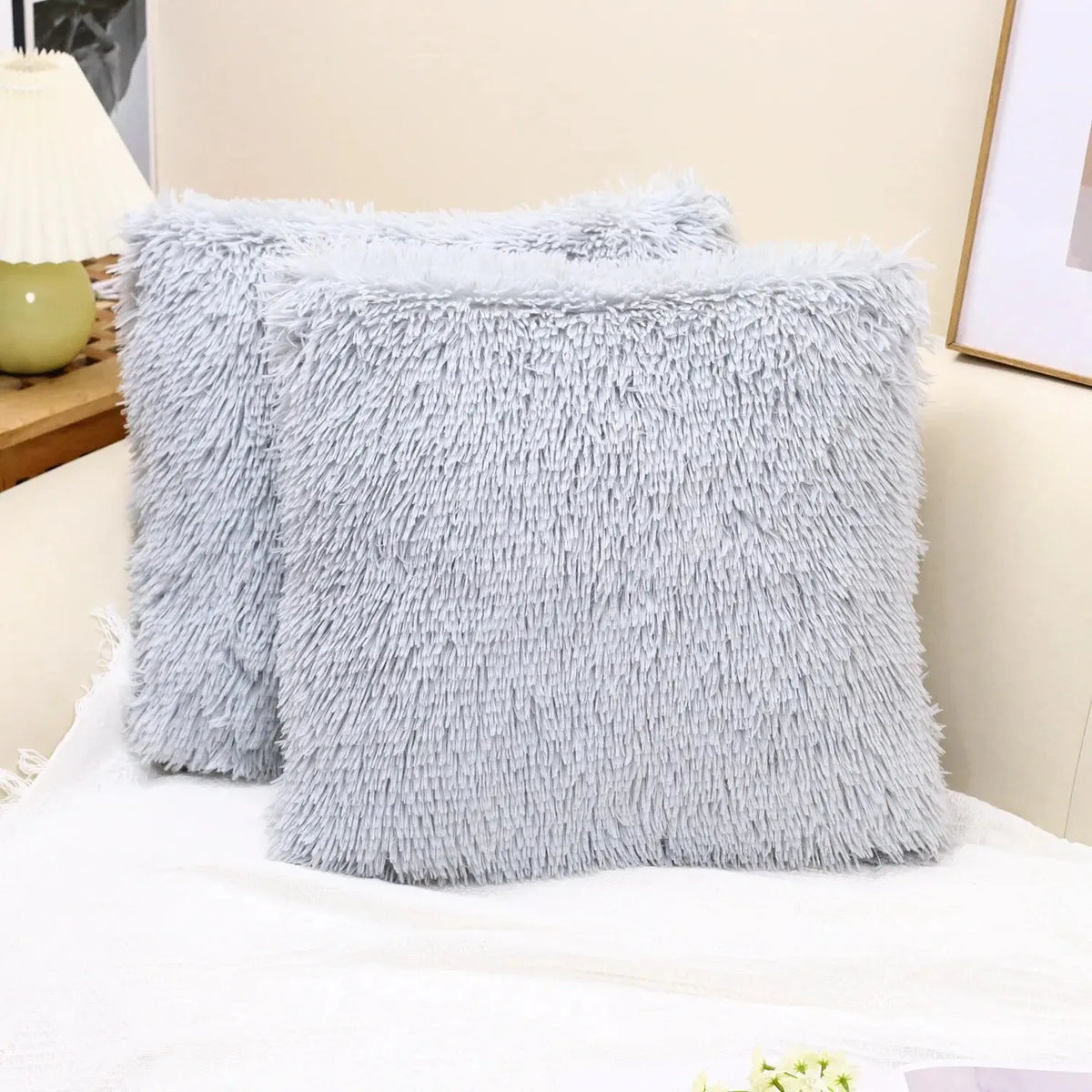 A stack of fluffy gray velvet throw pillow covers resting on a white surface.