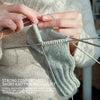 Hands are using a set of stainless steel knitting needles to work on a knitted garment.