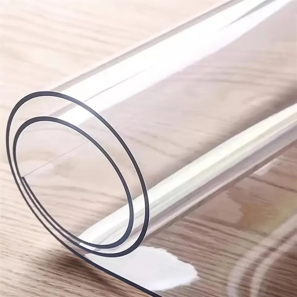 A clear PVC table protector mat rolled up on a wooden surface.