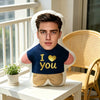 A man's face is printed on a soft, white pillow with a dark blue shirt and gold heart detail.