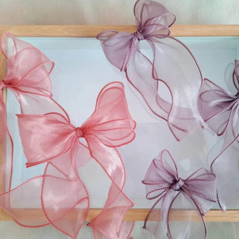 Pink and purple organza ribbons tied in bows displayed in a wooden frame for crafting