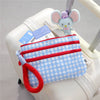 A light blue checkered waterproof passport holder with a pink strap and an elephant-themed charm is shown on a white rolling 