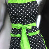 A black polka dot apron with bright lime green trim and ruffle details displayed on a mannequin.