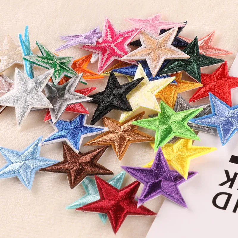 A collection of 20 five-pointed star embroidery patches in various colors and shades scattered on a light background.