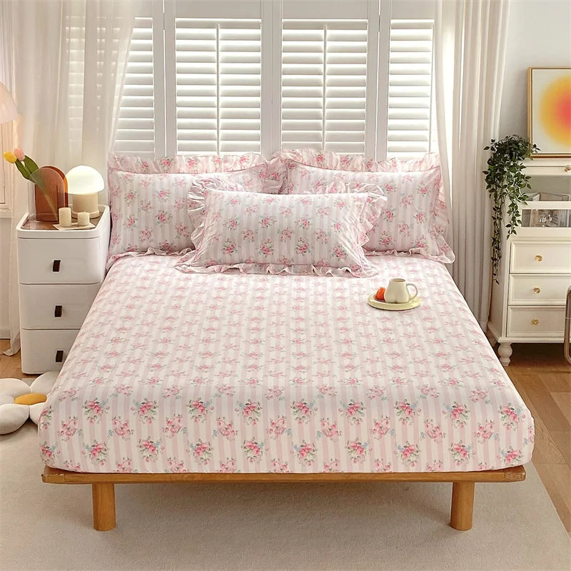 Pink floral printed cotton fitted sheet displayed on a bed with white linens and sheer curtains.