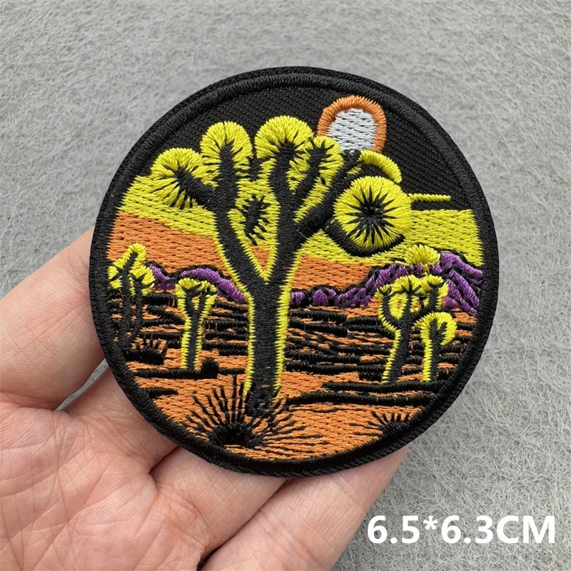Embroidered patch featuring a stylized tree silhouette against an orange sunset background.