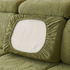 A close-up of a moss green sofa slipcover featuring a textured leaf pattern and a square white cushion.