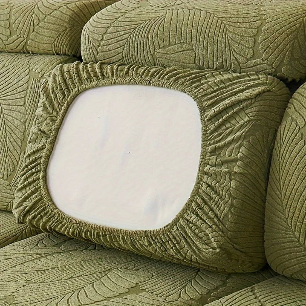 A close-up of a moss green sofa slipcover featuring a textured leaf pattern and a square white cushion.