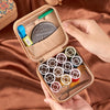 A hand holds an open tan storage box containing a retro style zipper sewing kit with various needles and tools.