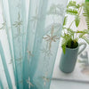Light blue sheer curtains with silver floral wave embroidery hanging in a window.