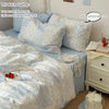 A set of three light blue floral duvet covers and pillowcases displayed on a bed with a white cake.