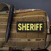 A tactical olive green fabric pouch featuring a black pen and a yellow sheriff embroidered patch.