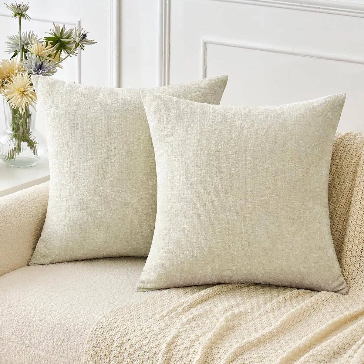 A beige chenille throw pillow cover resting on a light-colored sofa with a cream knit blanket.